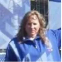 Smiling woman in blue jacket outdoors with long curly hair and a blurred background.