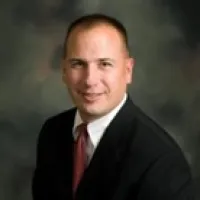 Professional businessman in suit and red tie smiling against a dark blurred background.