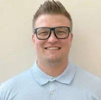 Smiling young man with short spiked hair and black glasses wearing a light blue polo shirt.
