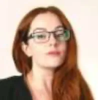 Portrait of a woman with long red hair and glasses wearing a black top against a light background
