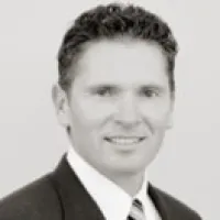 Black and white headshot of a man in a suit smiling against a plain background