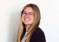 Portrait of a smiling woman with long blonde hair and glasses wearing a dark sweater against a white background