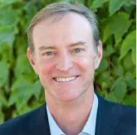 Smiling middle-aged man in a suit jacket with green leafy background outdoors