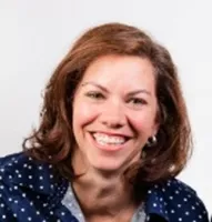Smiling woman with brown hair wearing a navy blue polka dot blouse against a white background