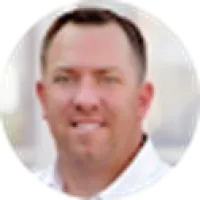 Portrait of a smiling man with short brown hair wearing a white shirt against a blurred background
