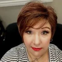 Woman with short auburn hair, red lipstick, striped shirt, and subtle makeup in an indoor setting