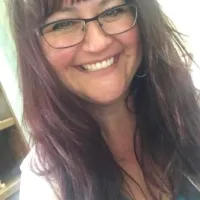 Smiling woman with long dark hair and glasses, showing a cheerful expression indoors.