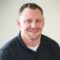 Smiling man with short hair wearing a black collared shirt against a plain light background