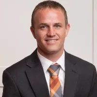 Professional man wearing a dark suit and patterned tie smiling against a plain background