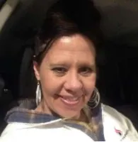 Smiling woman wearing large hoop earrings and a white jacket with a plaid collar inside a car at night