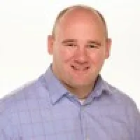 Portrait of a smiling bald man wearing a light blue checkered shirt against a white background