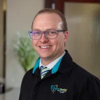 Smiling male dental professional wearing glasses and Langan Dental jacket in modern office setting.