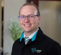Smiling male dentist wearing glasses and Langdon Dental jacket in a modern dental clinic reception area.