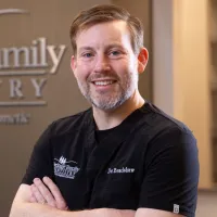 Smiling male dentist in black scrubs standing with arms crossed at Heritage Family Dentistry office.