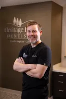 Smiling male dentist in black scrubs standing with arms crossed inside Heritage Hills Dentistry office.