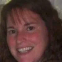 Close-up of a smiling woman with curly brown hair and bangs