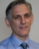 Portrait of a middle-aged man with gray hair wearing a blue dress shirt and tie, smiling slightly.