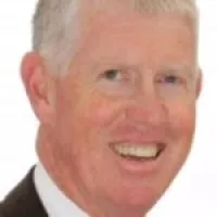 Smiling middle-aged man with short gray hair wearing a dark suit and white shirt against white background