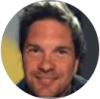 Close-up portrait of a smiling man with short dark hair in a circular frame with blurred background.