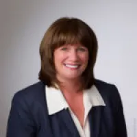 Professional woman with brown hair wearing a navy blazer and white collared shirt smiling against a gray background