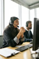 Two customer service representatives wearing headsets working at computers in a modern bright office.