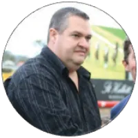 Man in black striped shirt standing outdoors with blurred green and yellow background in circular frame