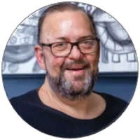 Smiling middle-aged man with glasses and a beard in a black shirt, with abstract art in the background.
