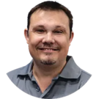 Smiling man with short dark hair and goatee wearing a gray collared shirt against a white background