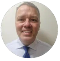 Smiling middle-aged man in a white shirt and blue tie against a plain light background.