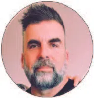 Close-up portrait of a middle-aged man with trimmed beard and short hair against a soft pink background.