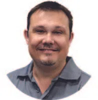 Smiling man with short dark hair and goatee wearing a blue collared shirt against white background