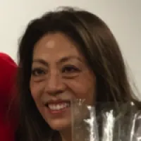 A smiling woman with long hair holding a clear vase, showing warmth and joy.