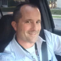 Smiling man in a car, wearing a white shirt, showing a friendly demeanor while driving.