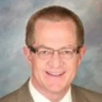 Smiling man in a suit with glasses against a soft, blurred background.