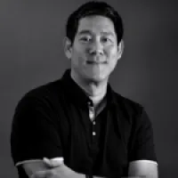 A smiling man with crossed arms, wearing a black polo shirt against a dark background.