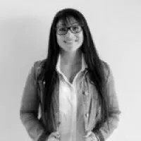 A young woman with long hair and glasses smiles, wearing a denim jacket over a white shirt.