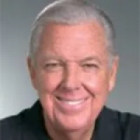 Smiling middle-aged man with gray hair, wearing a black shirt against a neutral background.