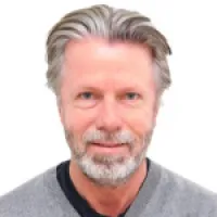 Smiling man with gray hair and beard, wearing a sweater, facial expression friendly and approachable.