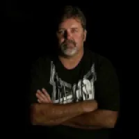 A man with crossed arms standing against a dark background, exuding confidence and strength.