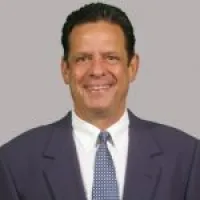 Business professional smiling in a suit against a neutral gray background.