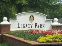 Entrance sign of Legacy Park surrounded by colorful flowers and greenery with brick pillars on each side.