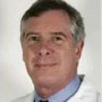 Portrait of middle-aged man with gray hair wearing a light blue shirt and white coat against white background