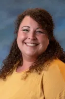 Smiling woman with curly hair wearing a yellow top against a soft blue background portrait