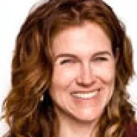 Smiling woman with curly red hair and light skin against a plain white background
