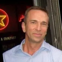 Man in light blue shirt standing inside near a neon star sign on a dark background