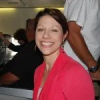 Smiling woman wearing a bright pink jacket sitting indoors with people in the background