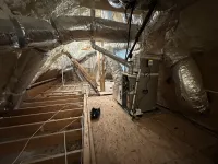 Insulated attic space with HVAC unit and ductwork wrapped in foil insulation on wooden floor framing.