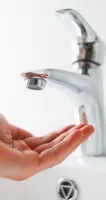 Fluctuating Temperature Hand held under a modern silver faucet over a white sink ready to catch water flow.