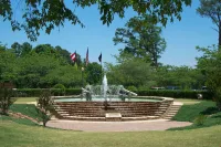 Peachtree City in Georgia. Outdoor tiered fountain with water jets in a park surrounded by trees and flags under clear blue sky.