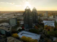 Sandy Spring King and Queen aerial view of skyscrapers and surrounding buildings with autumn trees under a setting sun sky.